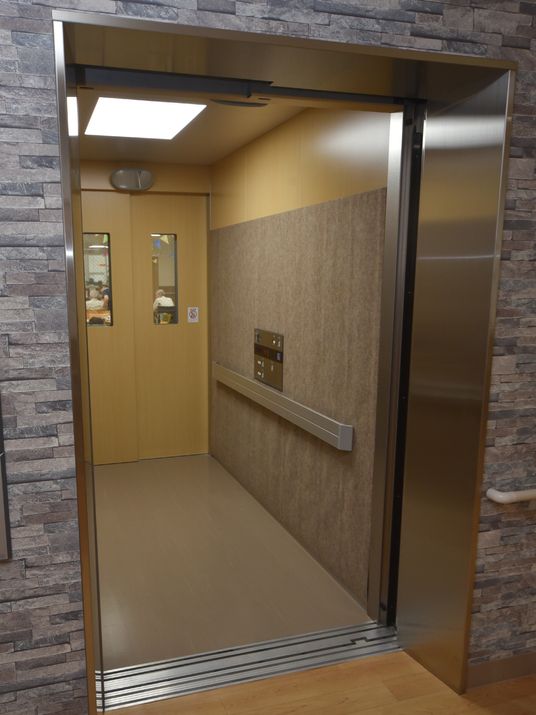 施設の写真 エレベーターの乗り口付近の壁が、石を積み上げたようなデザインになっている。手すりが壁に取り付けてある。