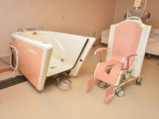 足腰の悪い人が、座ったままでも入浴ができる介助用のバスタブが置いてある。椅子はピンクで車輪がついている。