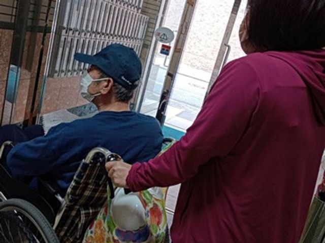 車椅子利用者の様子 エントランス 自然光が差し込むエントランスで、スタッフが車椅子利用者をサポートしています。温かい雰囲気です。
