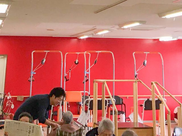 明るい機能訓練室 機能訓練室 赤を基調とした明るい空間で、利用者がリハビリに取り組んでいます。スタッフがサポートしています。