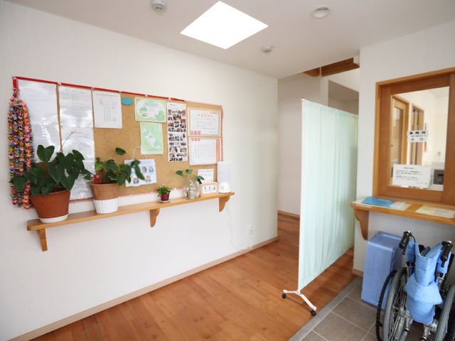 エントランスの明るい風景 玄関 心を和ます観葉植物が置かれたエントランスです。掲示板の情報も充実しており、働くスタッフにとっても有益な環境と言えるでしょう。