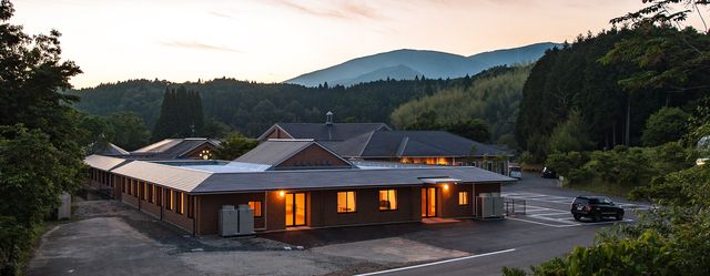 夕暮れ時の大きな建物の外観 外観 山に囲まれた穏やかな環境で、心地よい自然の中で働くことができます。