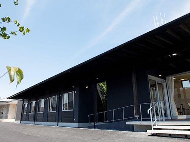 黒い外壁の建物外観 外観   黒い外壁が印象的な平屋の建物です。出入口前にゆるやかなスロープがあり、出入りしやすい造りに見えます。
