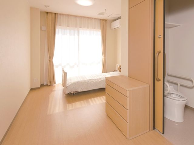 ベッドと自然光の居室 居室 広々とした居室は、木目調の落ち着いた雰囲気です。十分な自然光が入り、心地よく過ごせます。