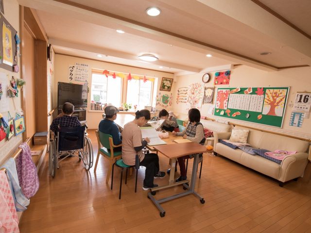 共有リビングの日常風景 共有スペース 様々なアクティビティを楽しんでいる居室の光景です。利用者の皆様がそれぞれの時間を過ごされており、温かい雰囲気が感じられます。