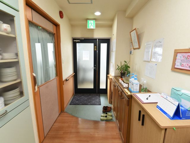 廊下と受付の様子 エントランス ゆったりとした廊下には明るい受付スペースがあり、来訪時に温かな対応を受けられる環境です。手元には清潔感の漂う物品が整然と並んでいます。