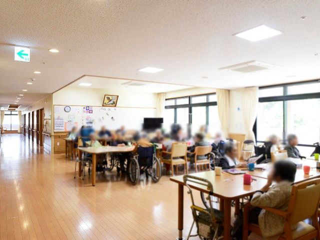 明るい共有スペース ラウンジ 自然光が差し込む広々としたラウンジでは、利用者が車椅子でゆったりと交流を楽しんでいます。
