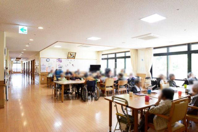 明るい共有スペース ラウンジ 自然光が差し込む広々としたラウンジでは、利用者が車椅子でゆったりと交流を楽しんでいます。