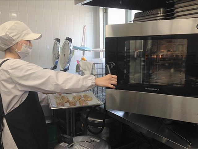 スタッフ作業中のキッチン キッチン 調理スタッフが機器を操作して、食事の準備を進めています。清潔で機能的な空間です。