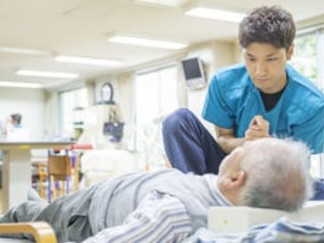 ケア中のスタッフと利用者の様子 内観 広々とした明るい空間で、スタッフが利用者に丁寧なケアを行っています。自然光が心地よく入ります。