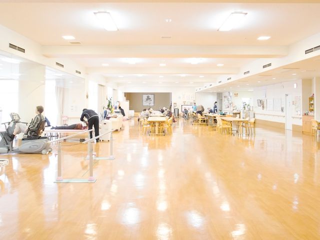 活気ある機能訓練室 機能訓練室 明るく広々とした空間で、多くの利用者がリハビリを行っています。自然光が心地よいです。