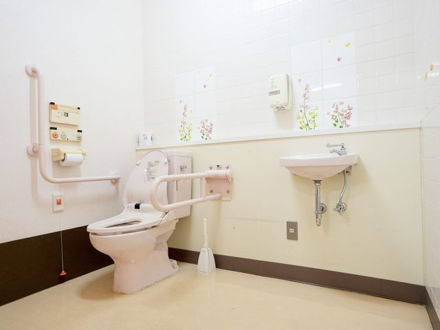手すり付きトイレ トイレ   手すりが複数あり、立ち座りを支えやすいトイレです。明るい壁面で、清潔感のある空間に見えます。
