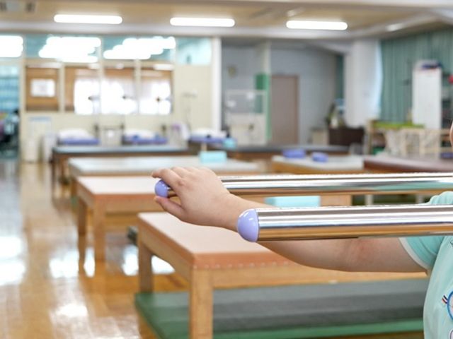 笑顔で機能訓練中の世代 機能訓練室 笑顔交わすスタッフと共に、明るく広々とした機能訓練室で体を動かす様子です。