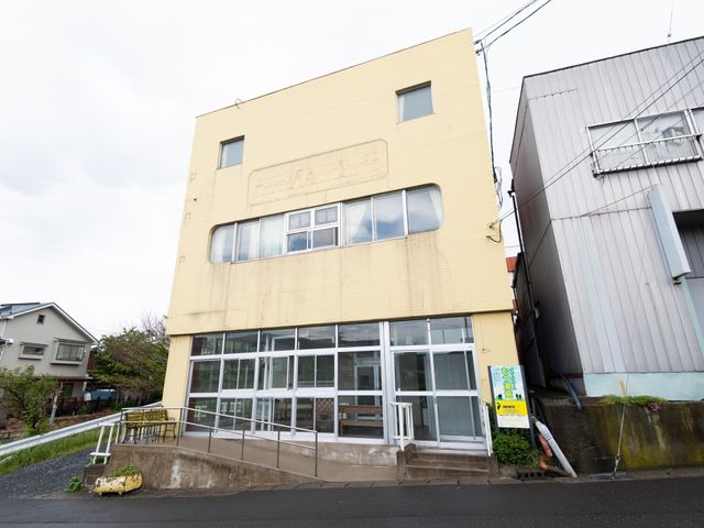黄色い建物のエントランス 外観 ガラス張りの明るいエントランスで、訪れる人を温かく迎えます。バリアフリー設計のため、どなたでも安心してご来訪いただけます。