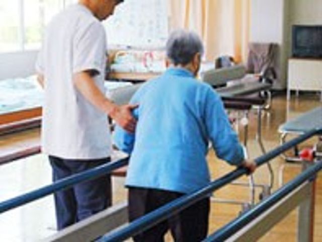歩行訓練中の様子 機能訓練室 利用者が施設スタッフと一緒に歩行訓練をしています。自然光の入る明るい空間で、安心してリハビリが行えます。