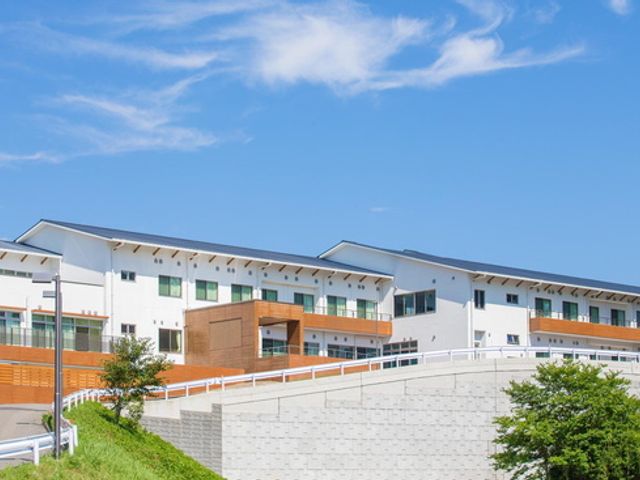 白い大きな建物 外観 青空と緑に囲まれた白い建物です。働く人々にとって心地よい職場環境が期待できます。
