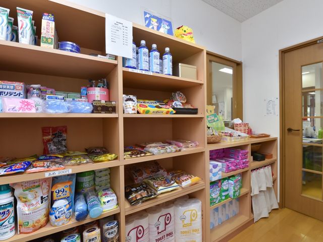 物品が並ぶ棚の様子 売店 日用品が豊富に揃う明るいスペースです。利用者の方々が日常の買い物を楽しめる環境が整っています。