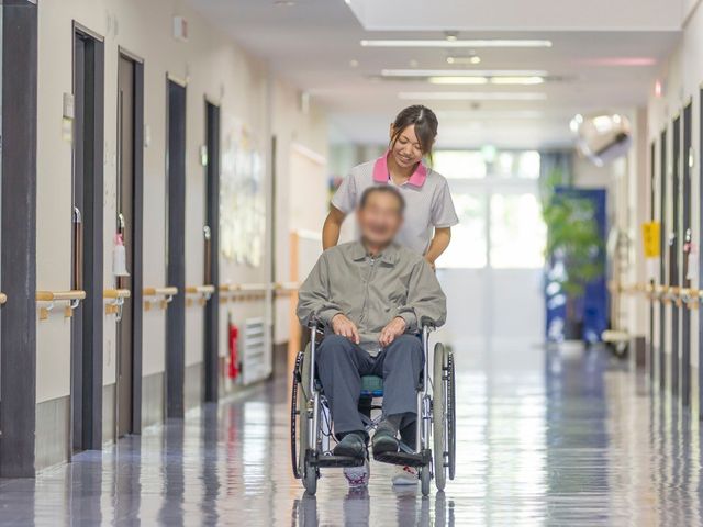 明るい長い廊下 廊下 広々とした廊下を車椅子で進む光景です。優しいサポートが感じられ、働くやりがいを見つけられます。