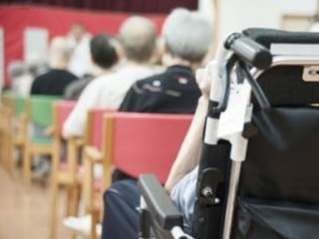車椅子の方々と共有スペース ラウンジ ゆったりとした共有スペースで、何人かの方が車椅子に座り、前方に何かに集中しています。安らぎと交流の場を提供している様子が伺えます。