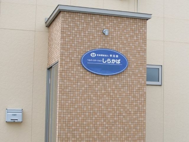 施設看板のある外観 外観   タイル調の壁に青い看板が設置された外観です。落ち着いた印象で、働く場所として建物の雰囲気をつかみやすいです。