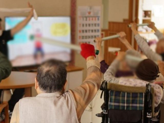 エクササイズ風景 機能訓練室 利用者の方々が、椅子に座って楽しみながらエクササイズをしています。