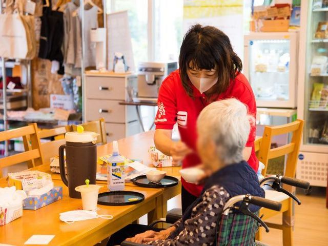 食事介助するスタッフ ダイニングルーム 明るいスペースでは、スタッフが高齢者の方に丁寧に食事のお手伝いをしています。落ち着いた雰囲気で安心して過ごせます。