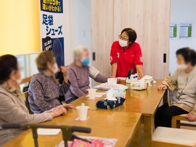 テーブルでの交流 ラウンジ 明るいラウンジで、スタッフと居住者がテーブルを囲んで親しげに交流しています。優しい空間で和やかな時間を過ごせます。