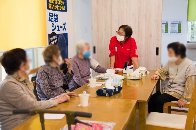 テーブルでの交流 ラウンジ 明るいラウンジで、スタッフと居住者がテーブルを囲んで親しげに交流しています。優しい空間で和やかな時間を過ごせます。