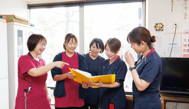 スタッフの打ち合わせ風景 スタッフイメージ 笑顔のスタッフが集まり、資料を見ながら打ち合わせをしています。自然光が差し込む明るい空間です。