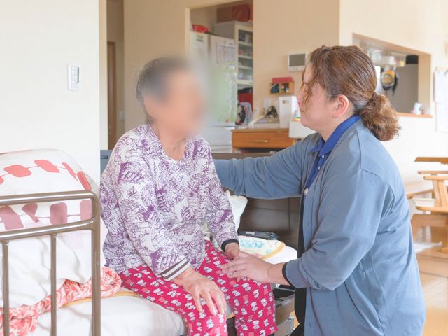 介護中の室内 居室 女性スタッフが入居者を優しくサポートしています。居心地の良い空間で、充実した時間を提供します。