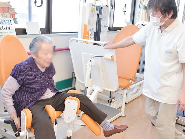 運動器具を使用する方 機能訓練室 自然光の差し込む明るい空間で、機能訓練が行われています。スタッフが優しくサポートしています。
