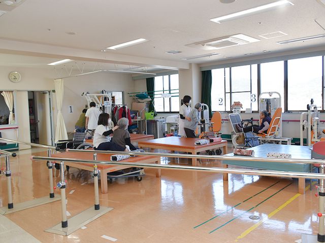 明るい機能訓練室 機能訓練室 開放的な空間で、利用者が器具を使ったリハビリに取り組めます。スタッフがサポートしています。