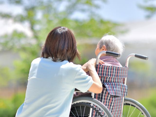車椅子利用者と介護士の様子 庭 自然豊かな環境で、介護士が利用者をサポートする姿が見受けられます。充実した日常が過ごせます。