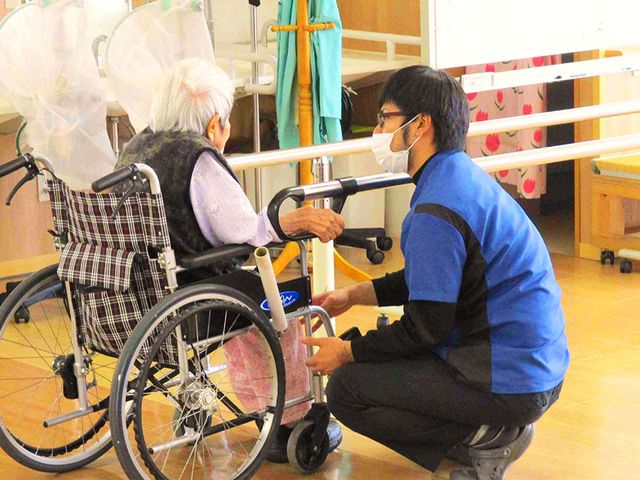 リハビリ支援の室内 機能訓練室 車椅子の方に、スタッフが親身にリハビリを支援しています。明るい室内で安心して作業できます。