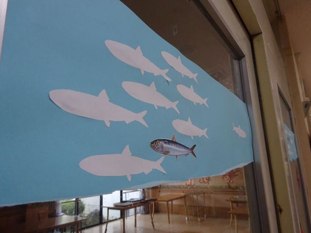 魚の飾りがある窓際の食堂 食堂   窓越しに魚の飾りが見える、明るい食堂です。テーブルが並び、落ち着いて食事や会話をしやすそうです。
