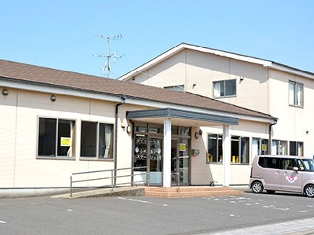 施設の正面外観 外観   白い外壁の建物で、入口前にスロープと手すりが見えます。車での来訪もしやすそうな、落ち着いたたたずまいです。