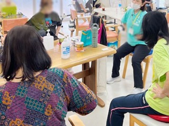 リビングでの交流 リビング 明るい空間で、利用者同士がテーブルを囲んで和やかに過ごしています。スタッフのサポートも充実しています。