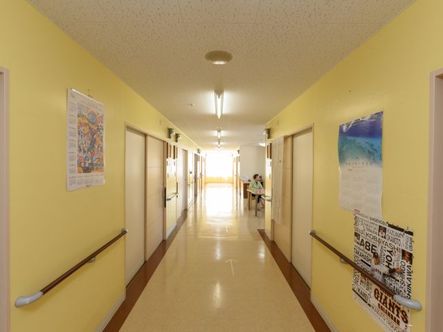 廊下の明るい風景 廊下 手すり沿いの温かみのある色彩で、安心感を与える明るい通路です。端に見える人物がリラックスしながら読書をしています。