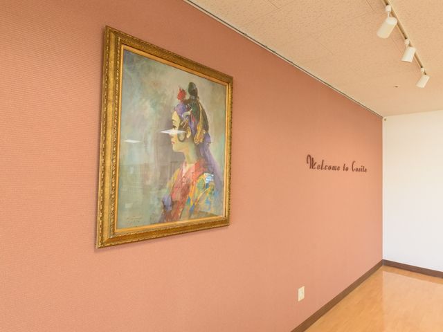 壁に絵画が飾られた廊下 談話室 温かみのある色合いの壁に、彩り豊かな絵画が飾られた落ち着いた雰囲気の廊下です。訪れる方々を優しく迎え入れる空間が広がっています。