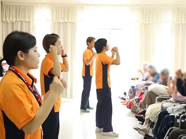 賑やかな機能訓練室 機能訓練室 明るい空間で、スタッフが高齢者と一緒に楽しく体操を行っています。新しいスキルも学べます。