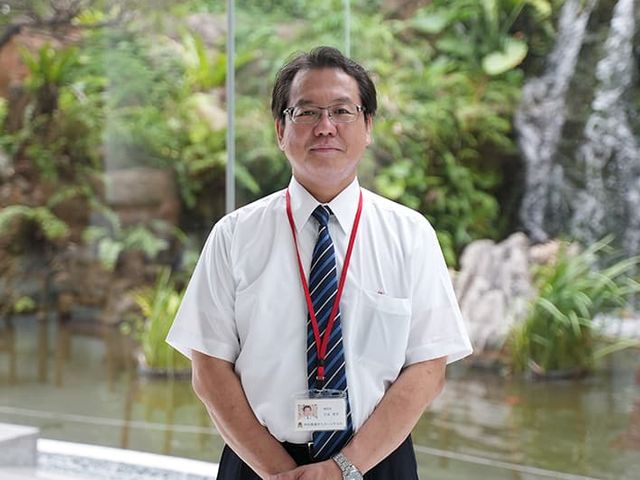 スタッフ立つ中庭 中庭 笑顔で立つスタッフがいる快適な中庭。心地よい自然光が降り注ぐ、開放的なスペースです。