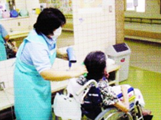 髪を乾かす場面の居室 居室 車椅子利用者の髪を乾かす、和やかな雰囲気の居室です。優しいケアが見えます。