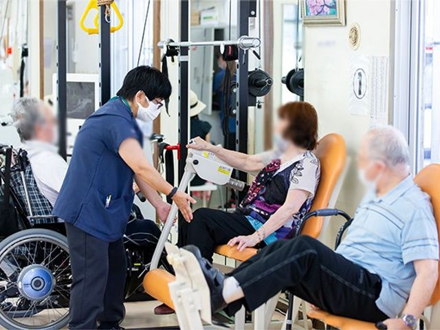 訓練を受ける人々の様子 機能訓練室 専門スタッフがサポートしながら、利用者がリハビリに取り組んでいます。明るく活気のある空間です。