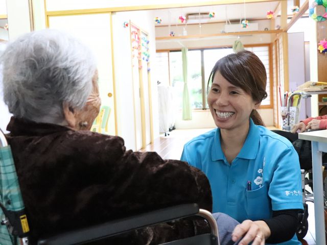 利用者と笑顔のスタッフの居室 居室   自然光あふれる暖かな空間で、利用者と笑顔のスタッフが対話を楽しんでいます。温もりに満ちています。