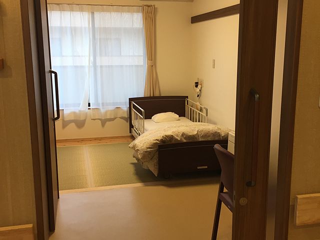ベッドがある和室の居室 居室   窓からやわらかな光が入る、落ち着いた和室の居室です。ベッドと畳の空間が分かれており、ゆっくり過ごしやすい印象です。