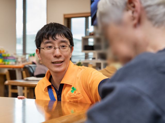 笑顔のスタッフと利用者 スタッフ 温かな笑顔で対話するスタッフがいる明るい空間です。ここでは利用者一人ひとりとのコミュニケーションを大切にしています。