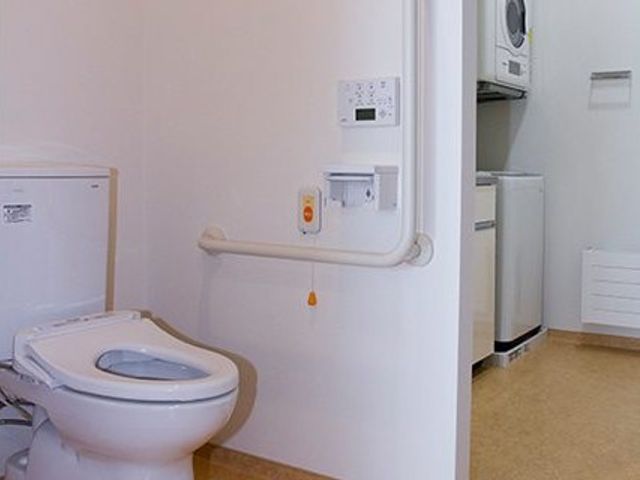 トイレと洗面台のある個室 トイレ   広めのトイレに手すりが設置されており、落ち着いた色合いで使いやすそうです。隣に洗面スペースも見えて、動線を確認しやすい空間です。