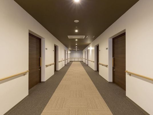 手すりと居室のドアが両サイドに設置された廊下。まっすぐでフロアの色は両サイドと中央の色が異なる。
