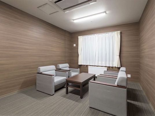 白い椅子が4脚セットされ、中央に木製のテーブルが置かれた部屋には大きな窓があり、カーテンが付いている。