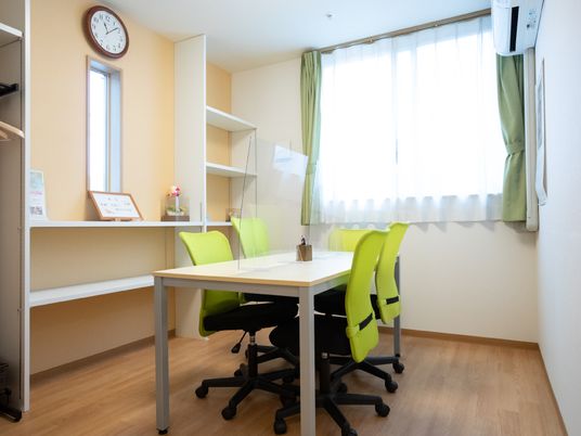 白い机と黄緑の椅子が置かれた白い壁の部屋
